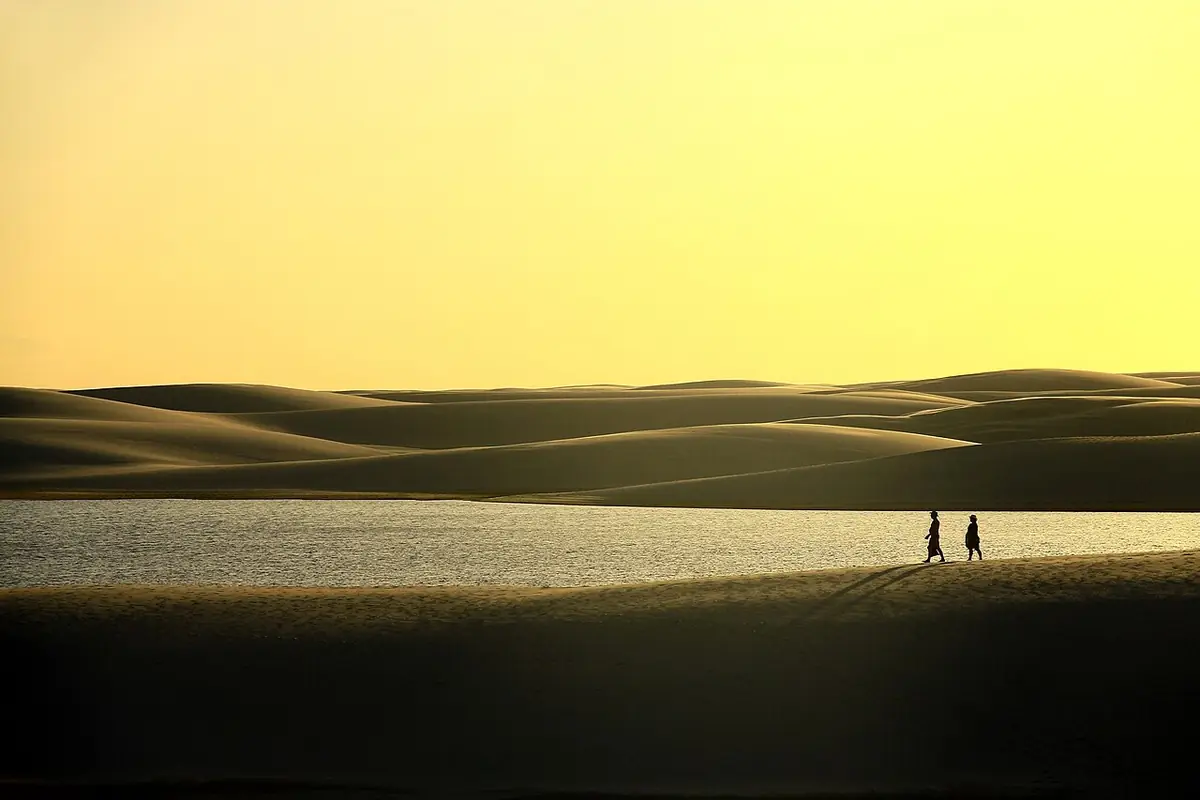 Casal caminhando entre as dunas e lagoas dos Lençóis Maranhenses ao entardecer